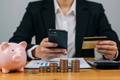 Mann mit Smartphone, Bankomatkarte, Sparschwein und Münzen